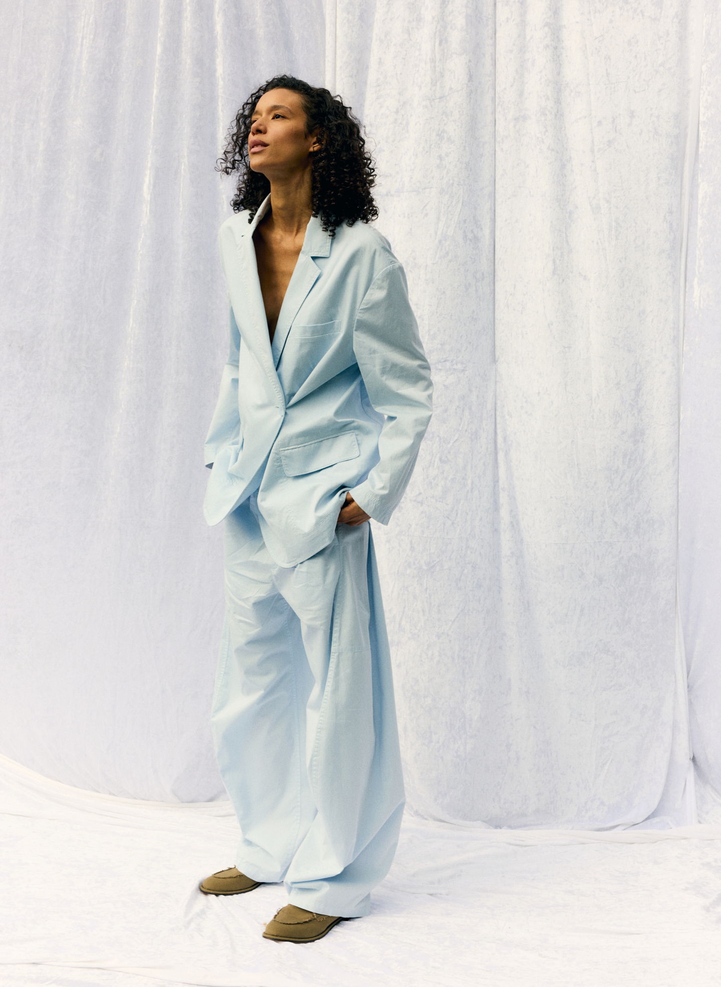 Model in oversized light blue suit against a plain backdrop.
