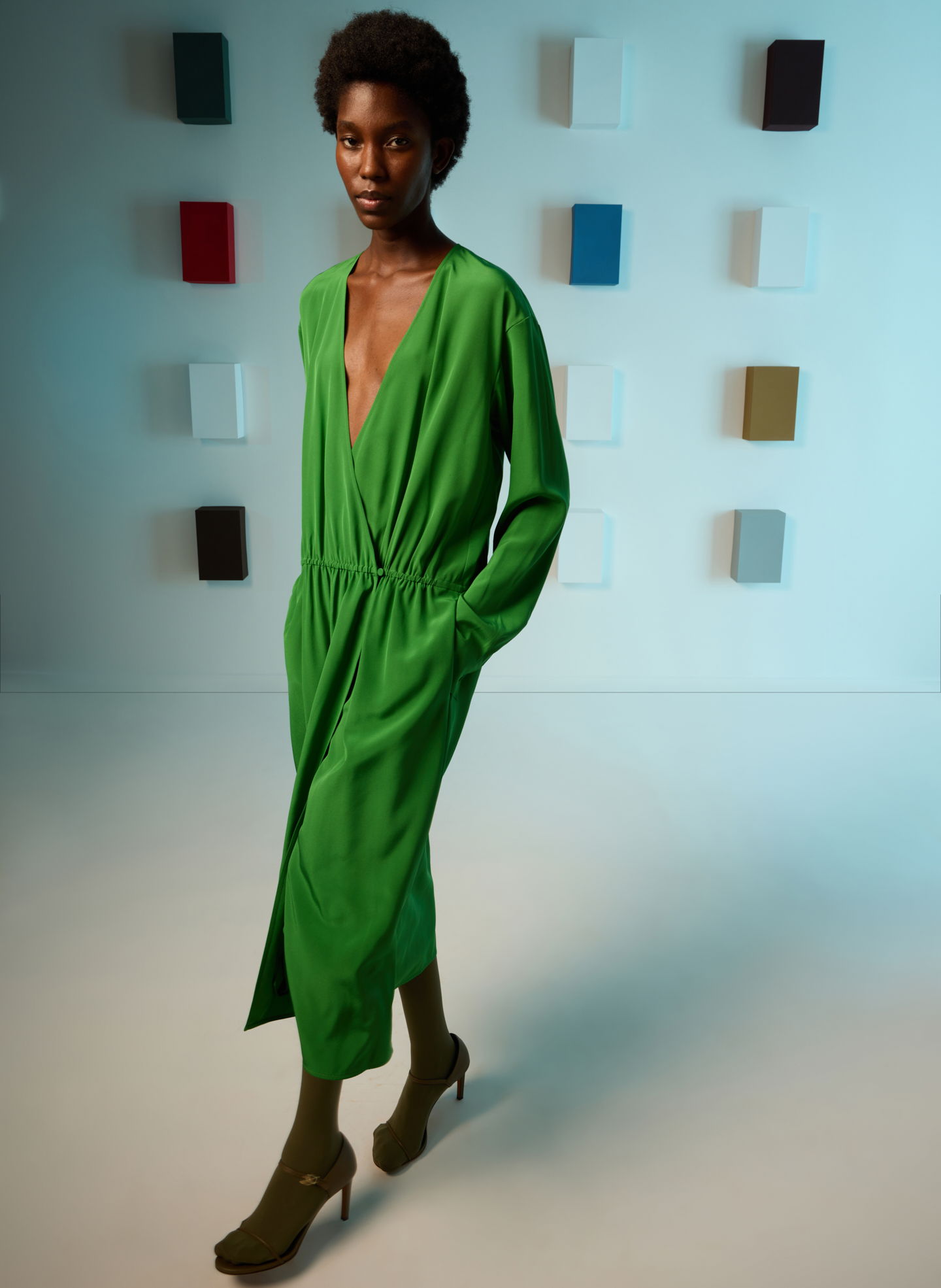 Model in a green dress walking against a colorful background.