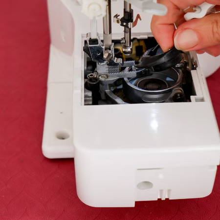 hand removing the shuttle hook from the bobbin compartment of a sewing machine