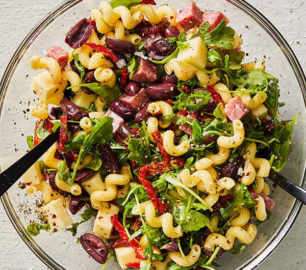 Cavatappi pasta with olives, tomatoes, arugula and cubed salami and provolone tossed in a glass bowl