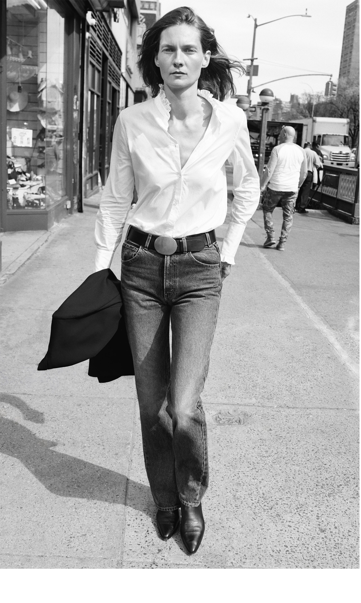 Person walking on a city sidewalk, wearing a white shirt and jeans.