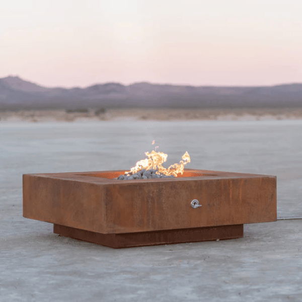 Low square steel gas fire pit with small flame in a desert landscape at dusk