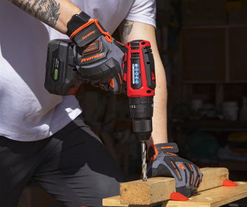 Person using a cordless drill on wooden planks while wearing gloves.