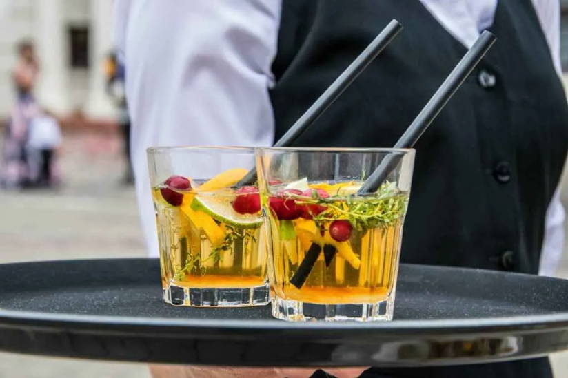 Image of waiter holding two orange drinks with fruit in them.