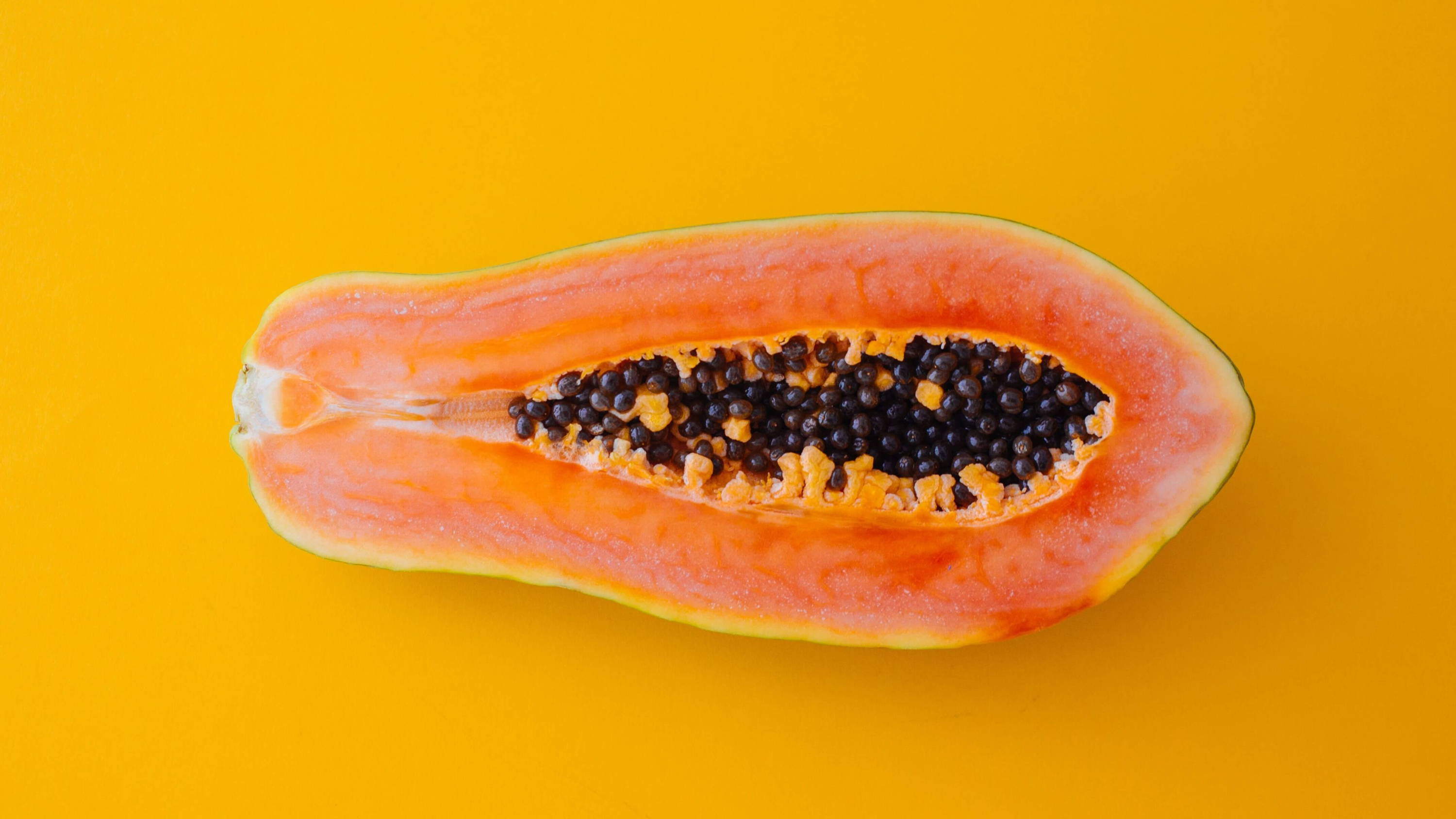 a halved papaya against a golden yellow background.
