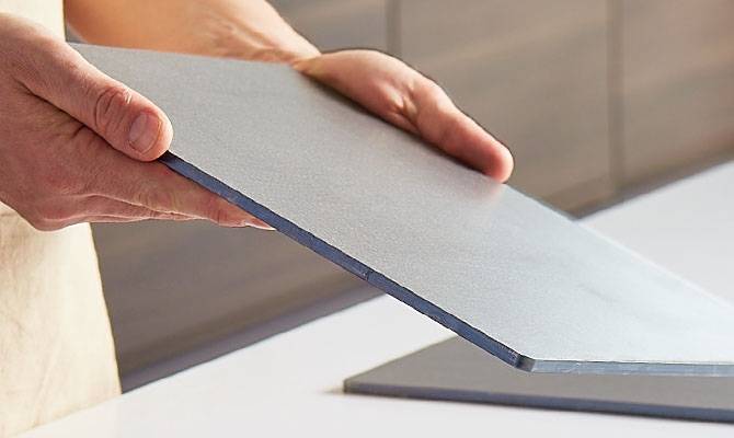 A chef holds a Misen Oven Steel in both hands with its edge facing the camera, showing its 6mm thickness.