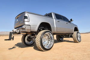 Rear three-quarter view of a lifted gray Dodge Ram 1500 Limited on chrome wheels in desert terrain