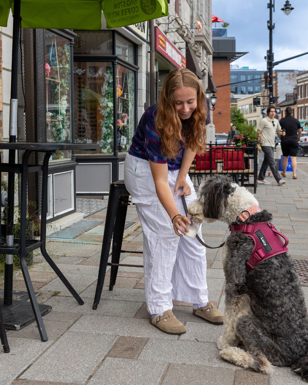 Young woman petting a dog outside a cafe on a city street.