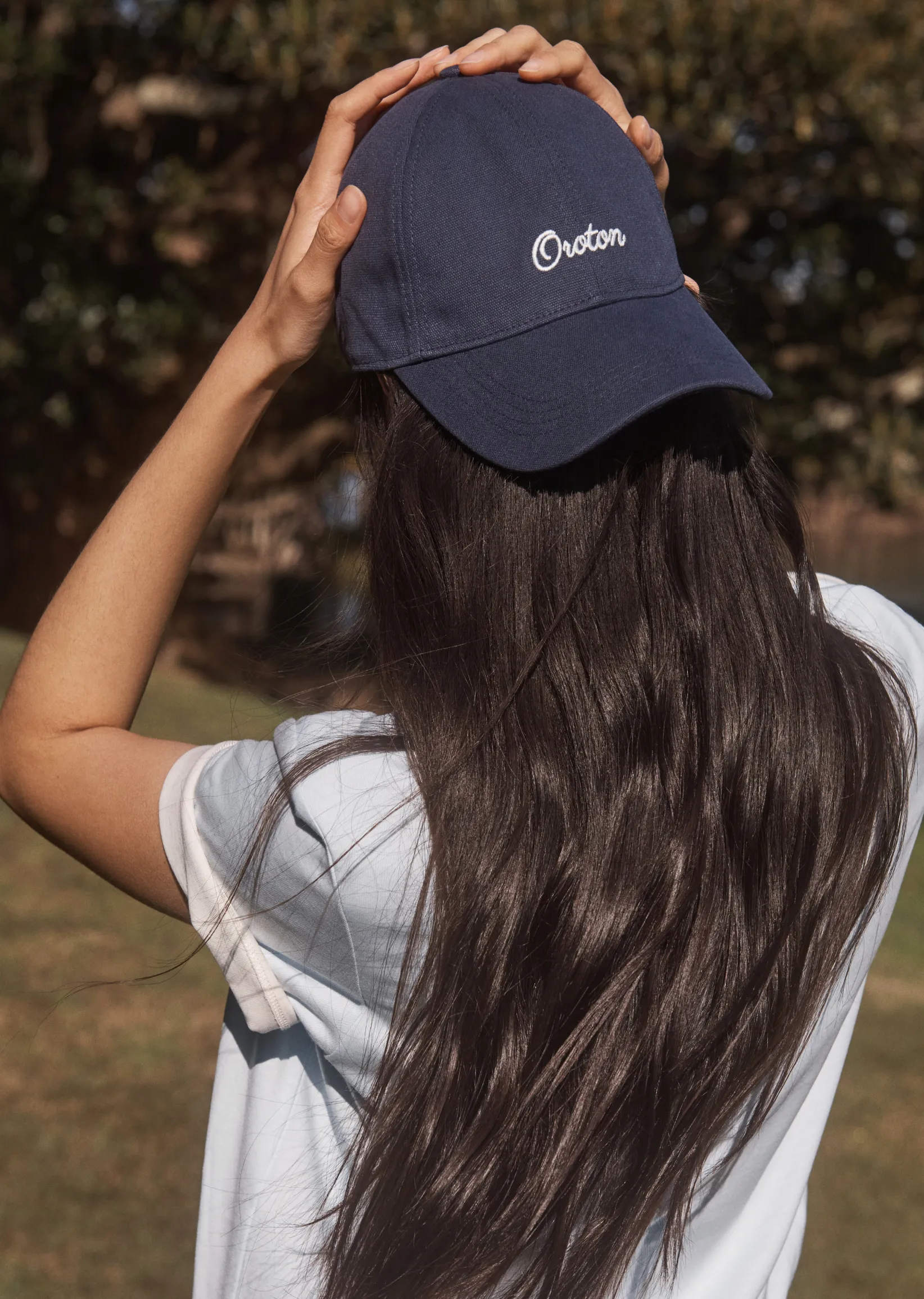 Person with long hair wearing a navy cap outdoors.