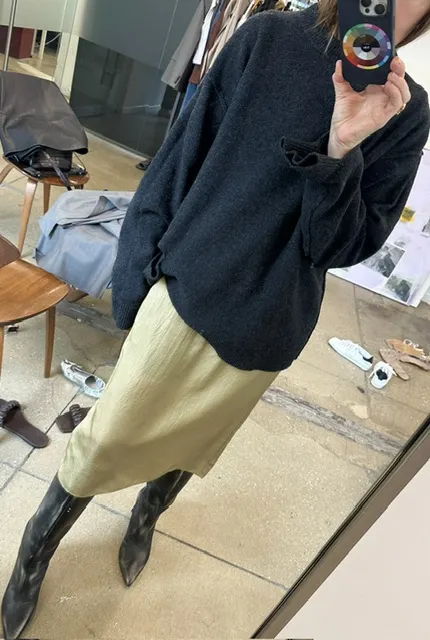 Person wearing a dark sweater, skirt, and tall black boots in a mirror.