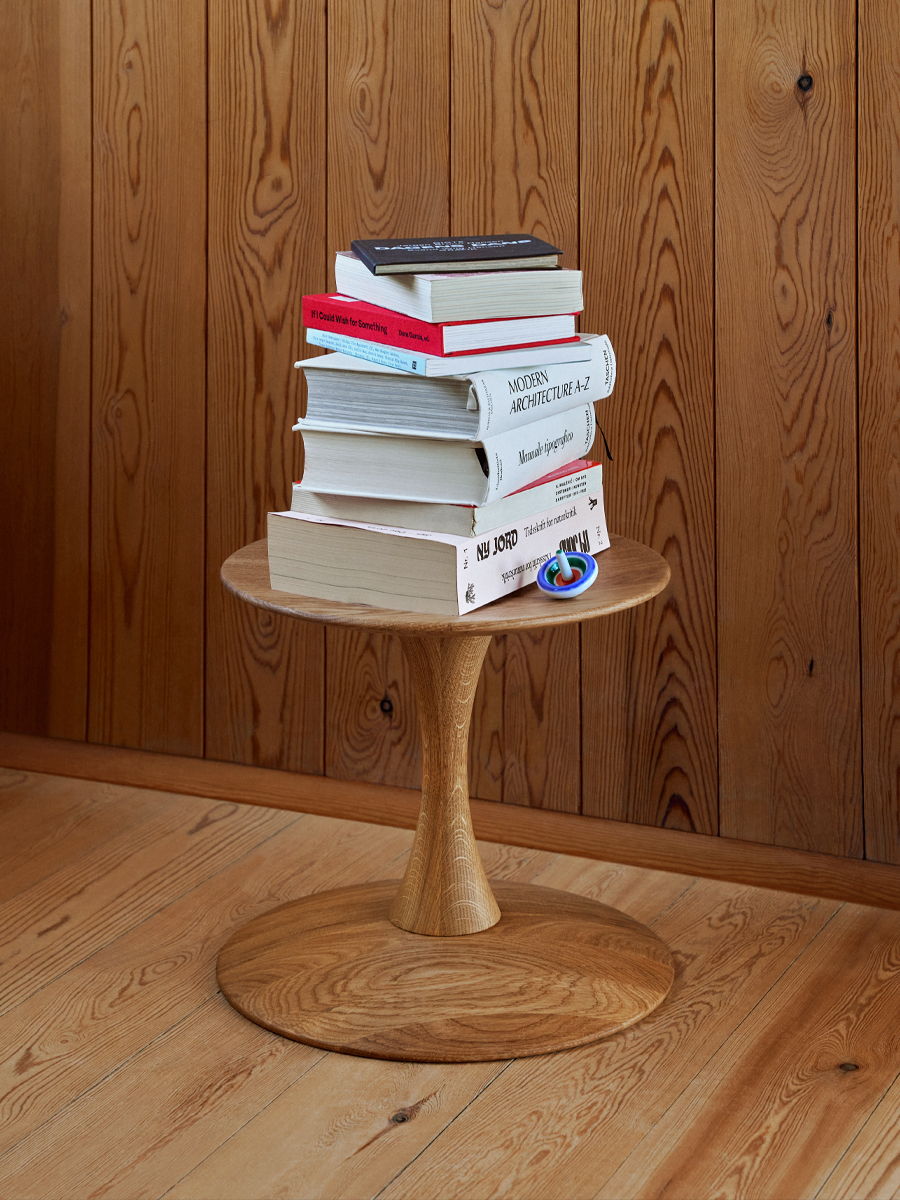 A wooden table with a stack of books on top, against a wooden wall.