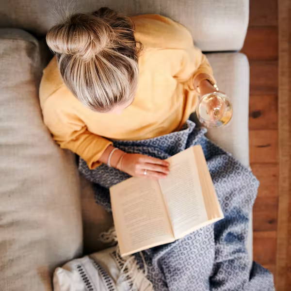Comfy woman reading on the sofa with a glass of wine