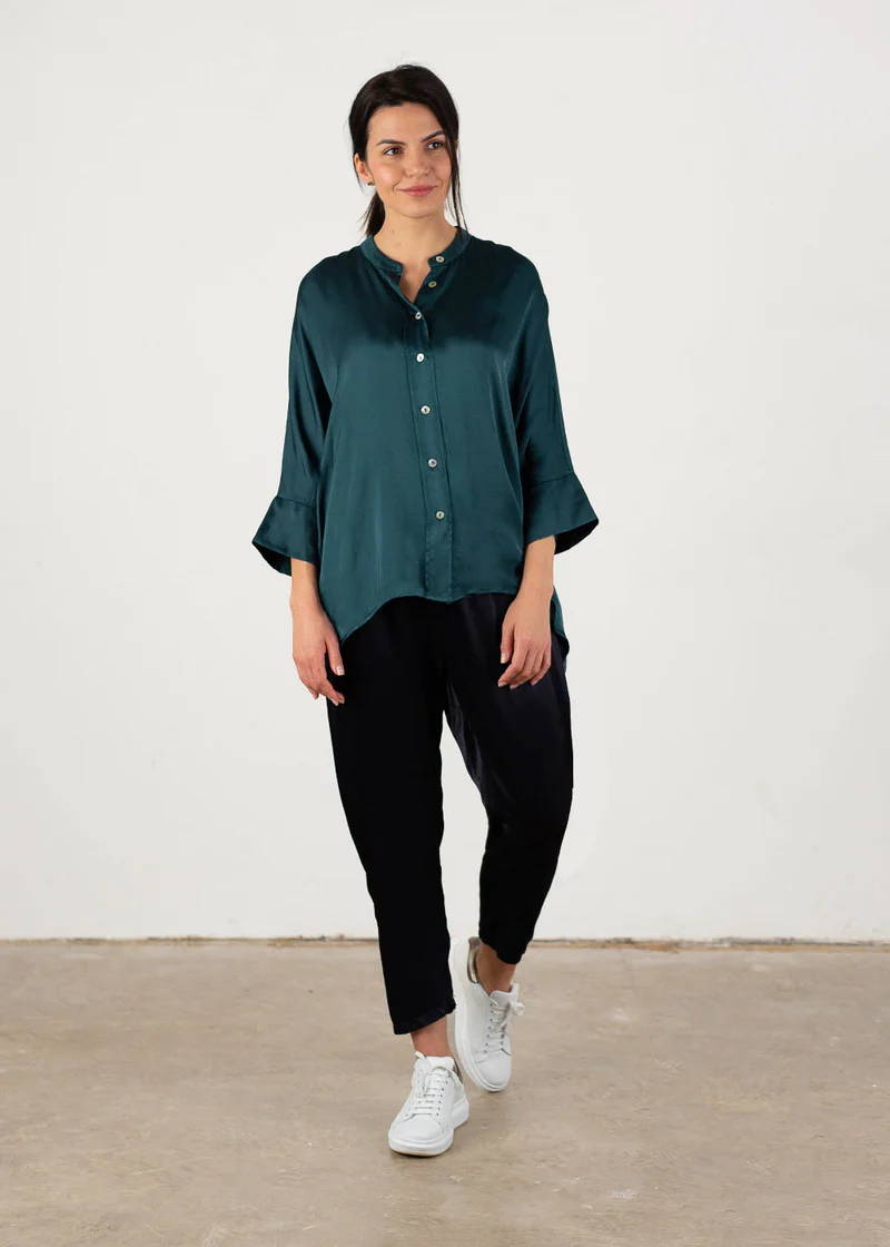 A model wearing s teal blue oversized satin shirt with black trousers and white trainers