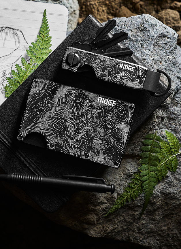 Ridge wallet and key holder on a rocky surface with fern leaves.
