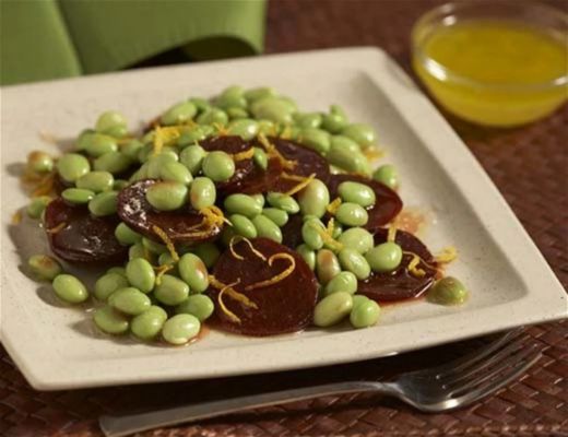 A plate of edamame beans with sliced sausage and lemon zest.