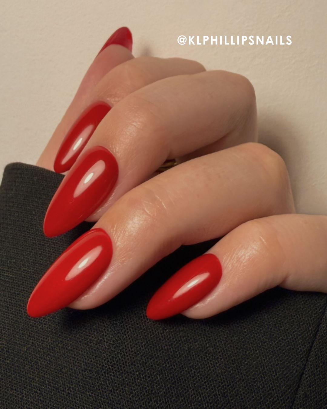 Hand with long red nails against a dark background.