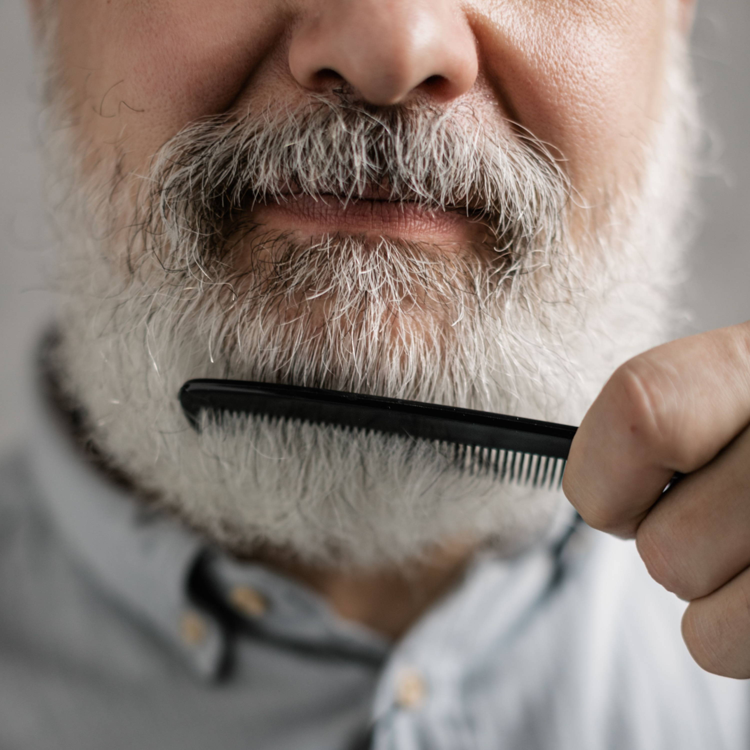 Man combing his beard while wearing a light blue shirt.