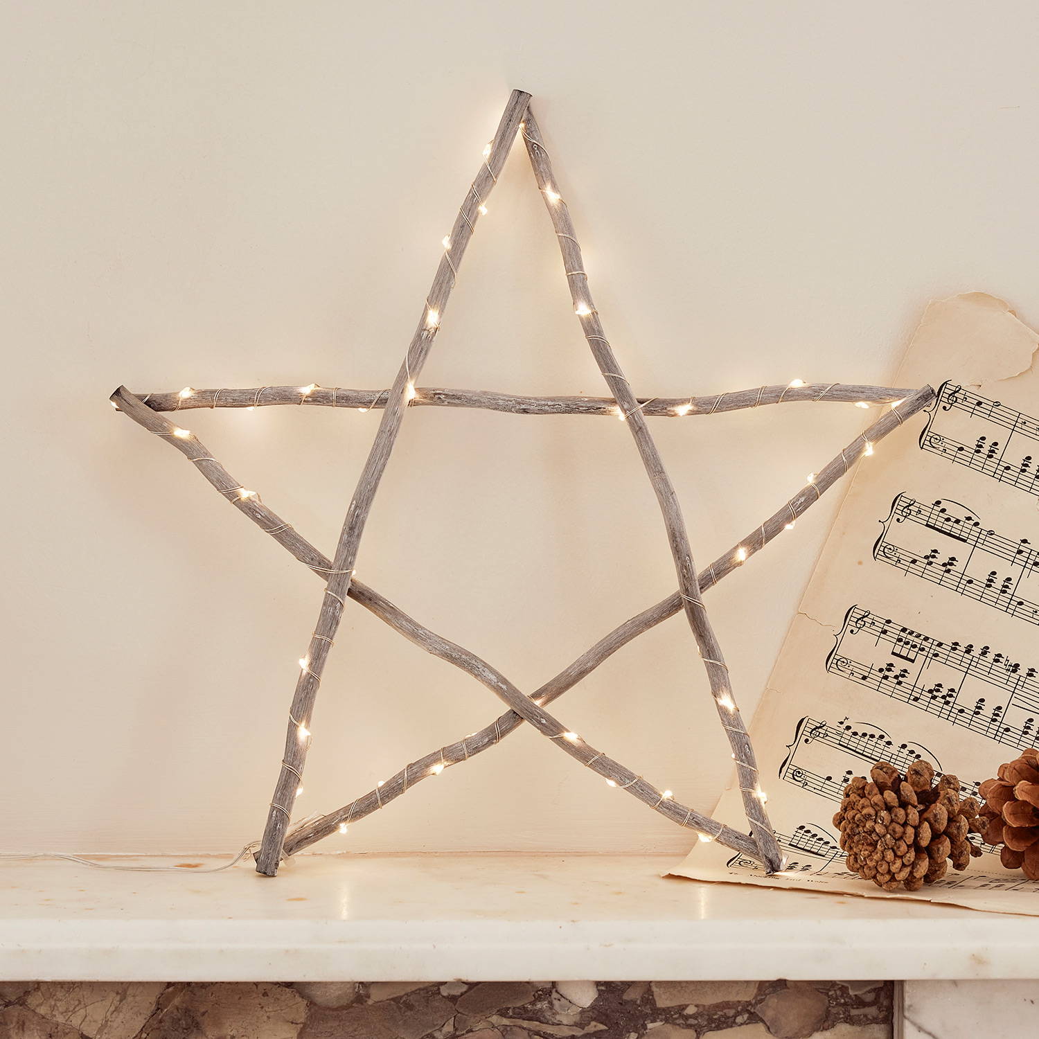 Grey wooden star light on a mantlepiece with pinecones and a song sheet. 