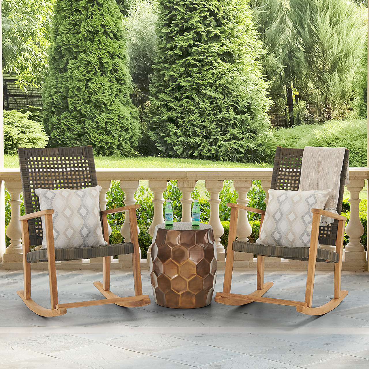 Two rocking chairs and a table on a patio surrounded by greenery.