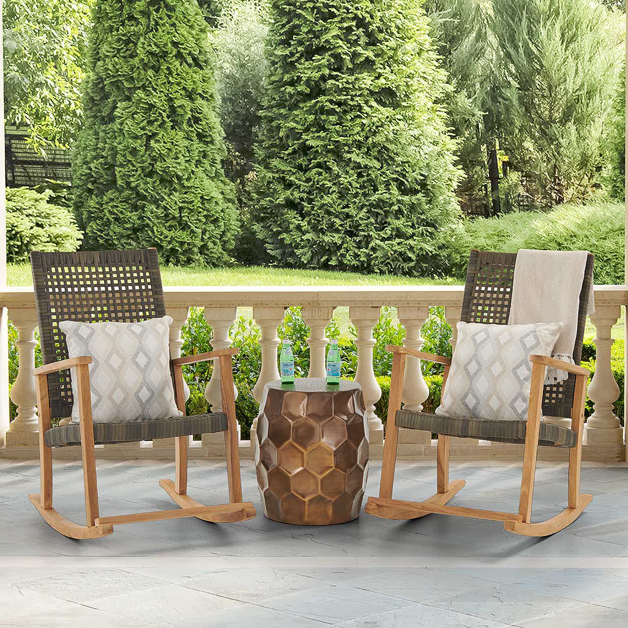 Two rocking chairs and a table on a patio surrounded by greenery.