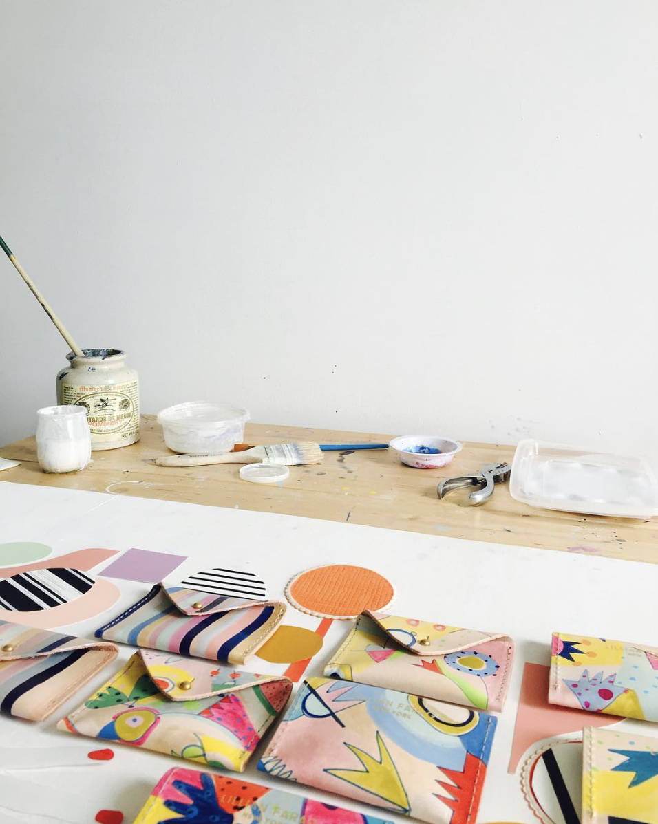 Artist's studio with paint and brushes and hand painted leather wallets in the foreground.