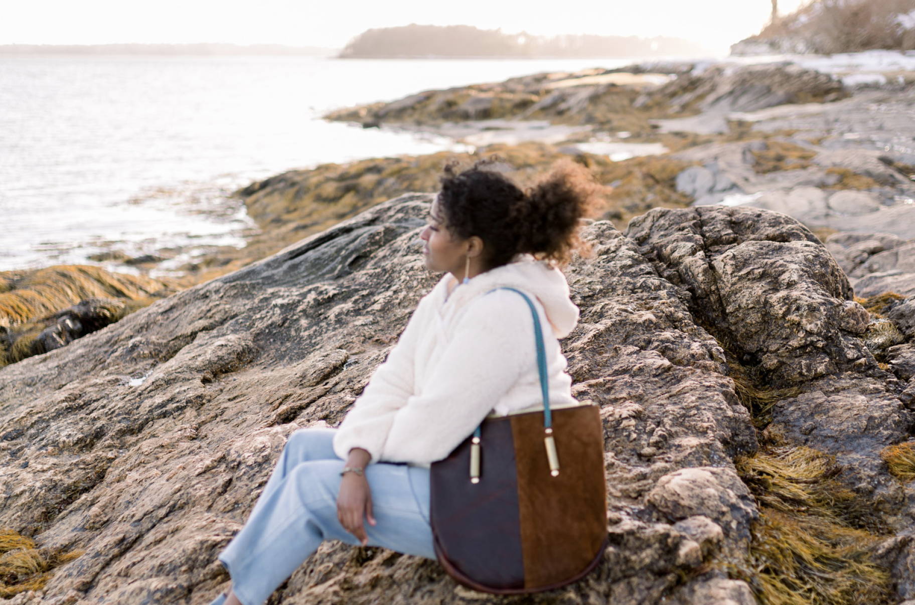 woman looking out on the rocky coast with a leather bag