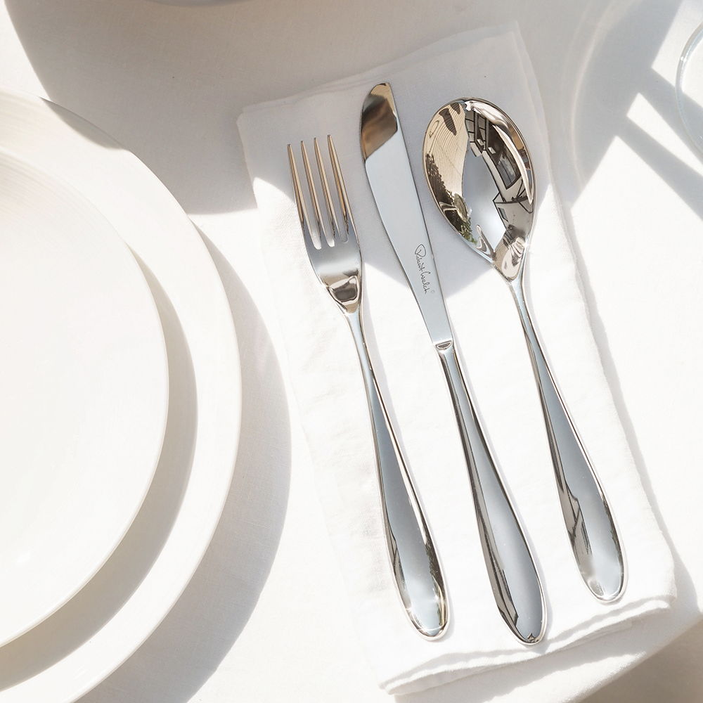 A Deta Bright fork, knife, and spoon arranged on a white napkin.