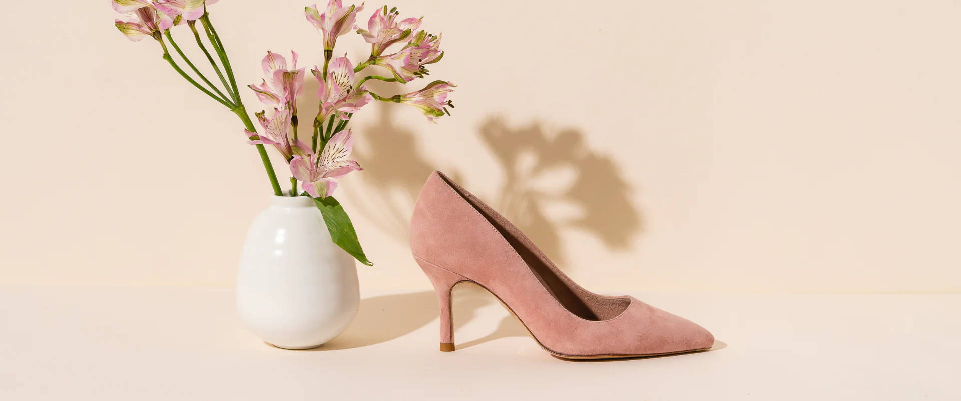 Pink high heel shoe next to a white vase with flowers.