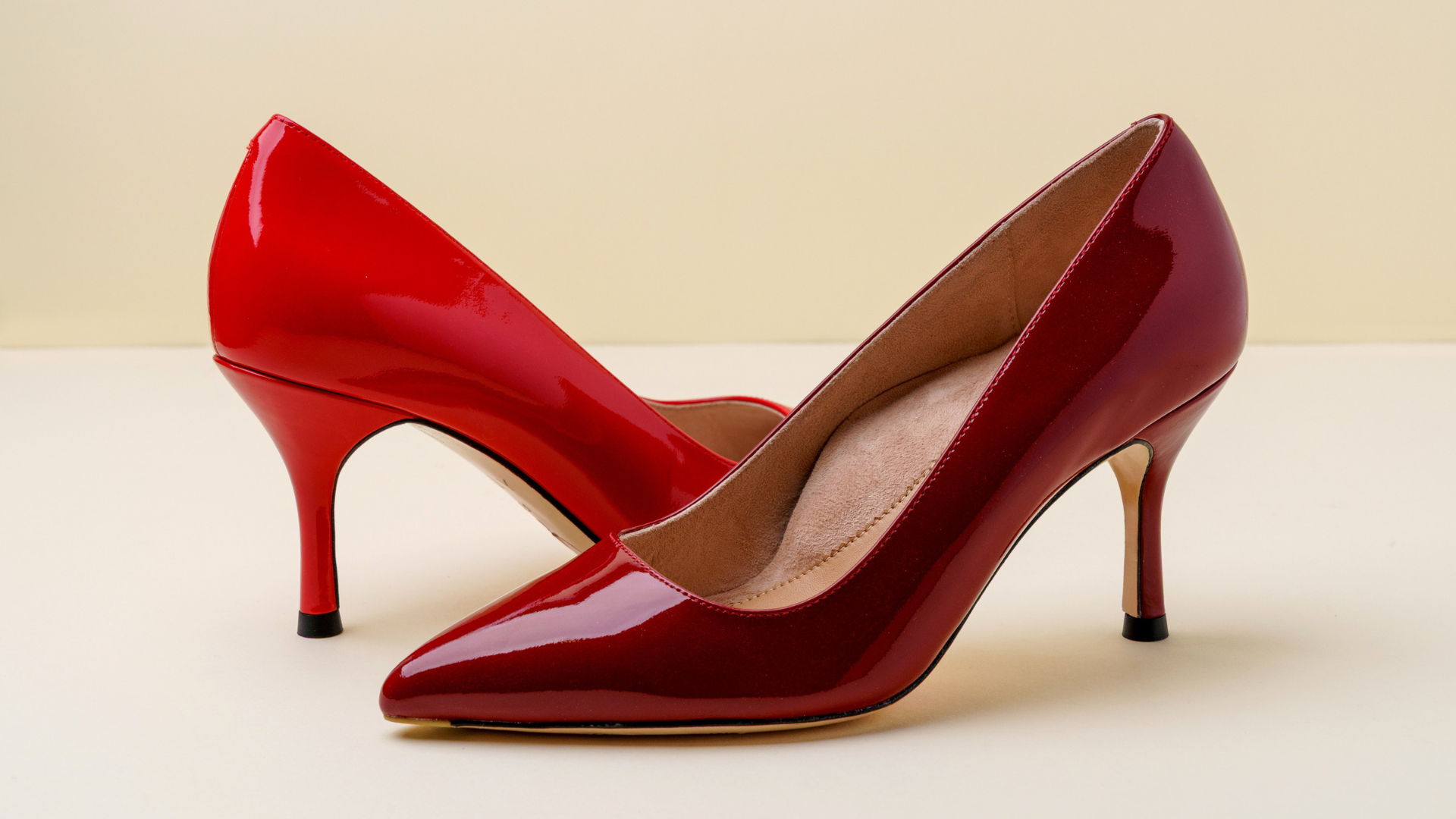 Two pairs of glossy red high heels on a light background.