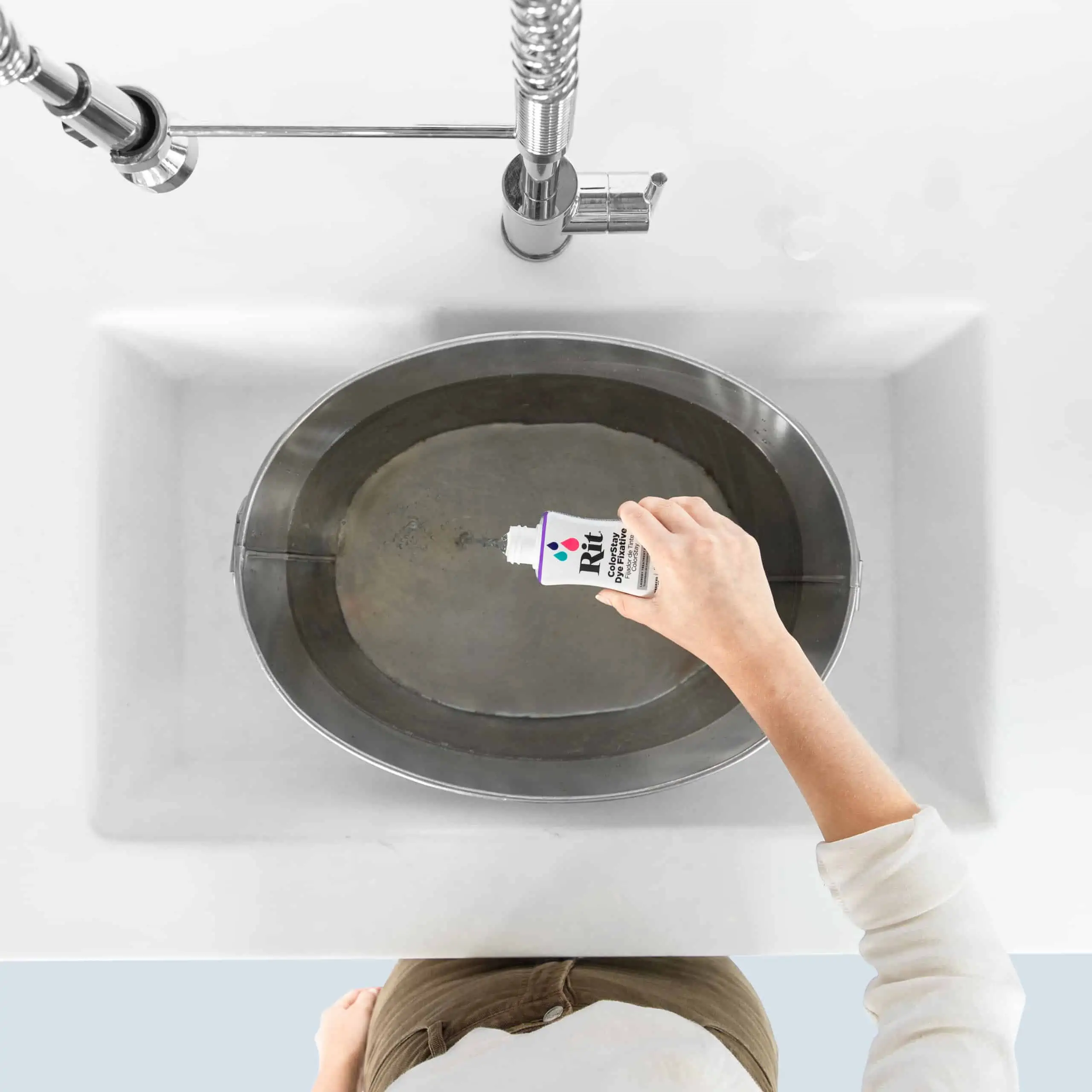 Hand pouring liquid into an oval sink from a small bottle.