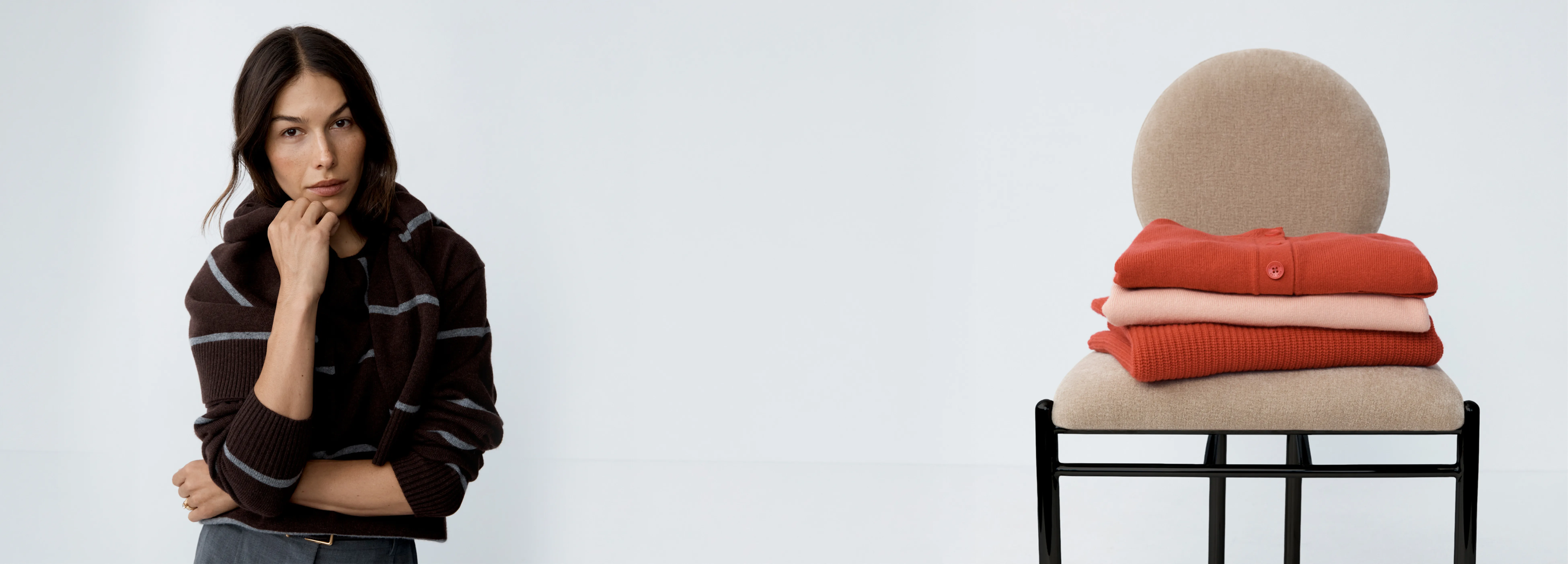 Woman posing next to a chair with stacked clothing on it.