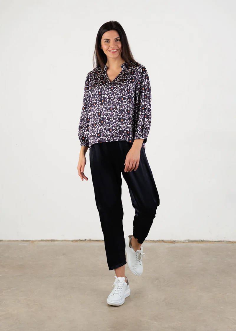 A model wearing an inky blue floral satin blouse with black trousers and white trainers