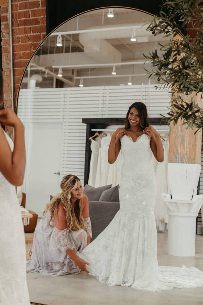 La mariée porte la robe Clo dans une salle d'exposition et le personnel ajuste la traîne.