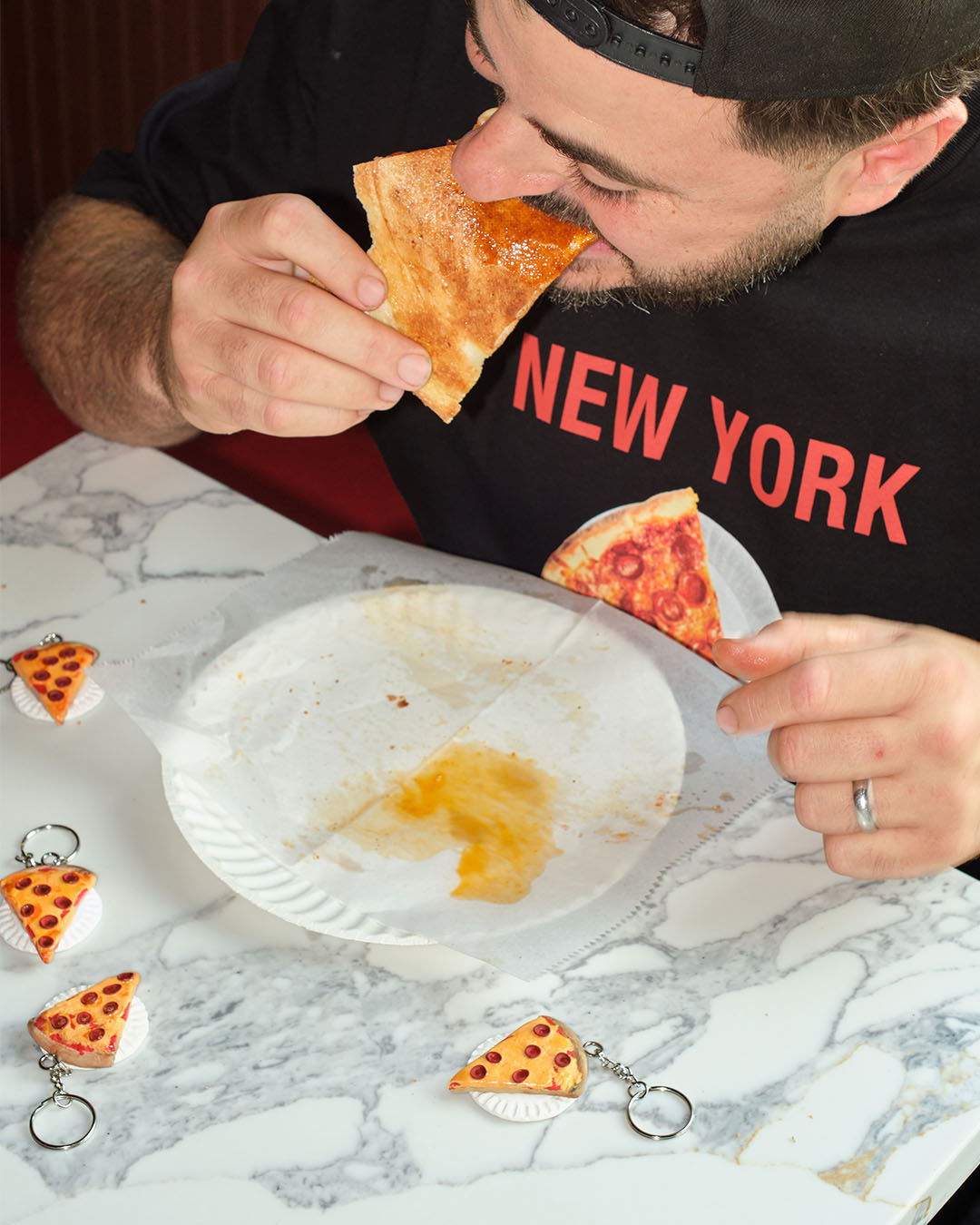 Person eating pizza with miniature pizza keychains on a plate.