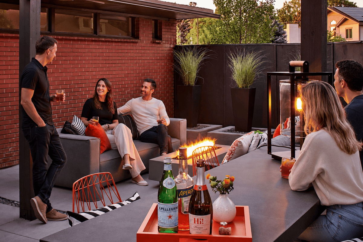 Friends conversing around a modern patio fire pit with outdoor bar seating and lounge furniture.