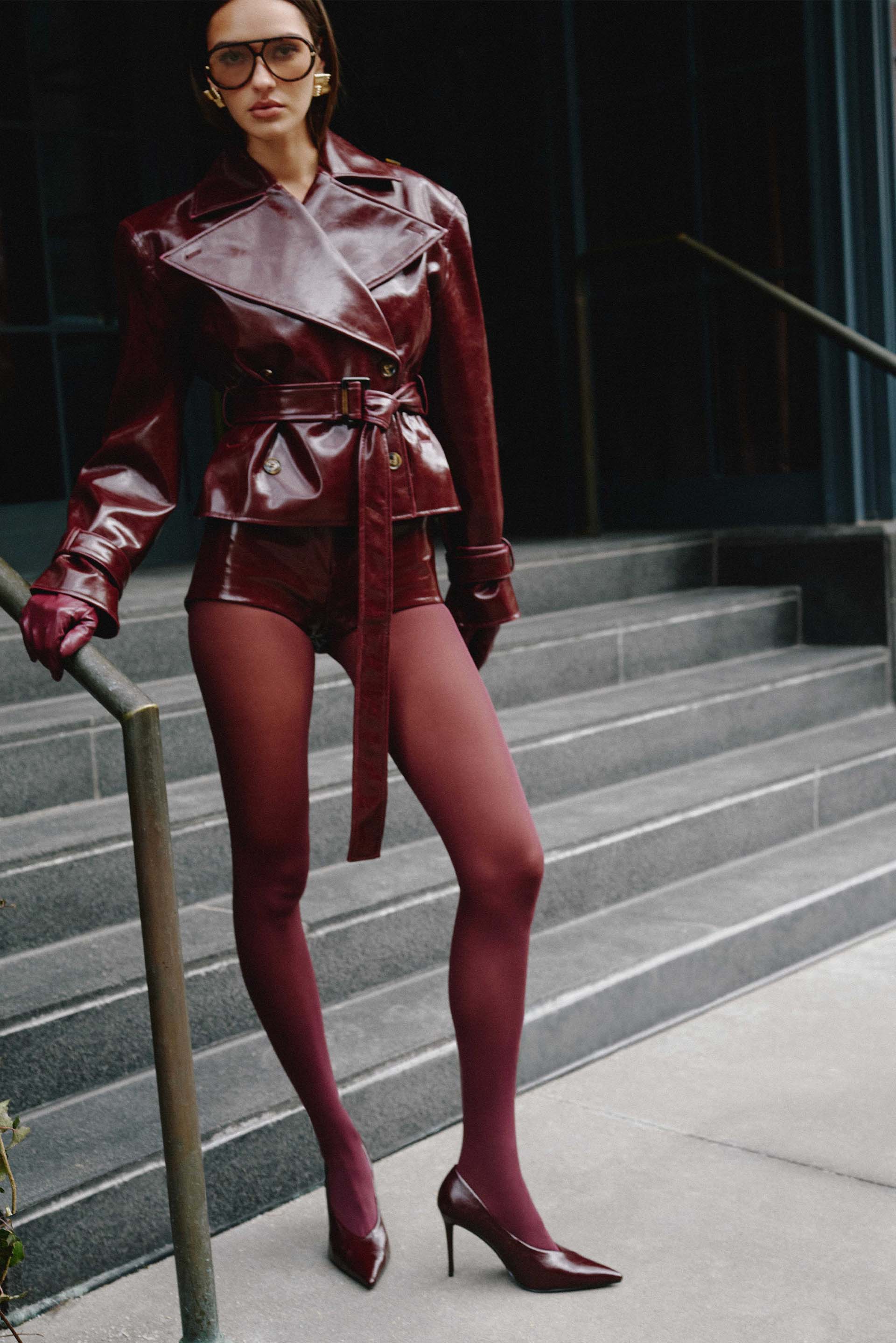 Model in a burgundy outfit with high heels, standing on steps.