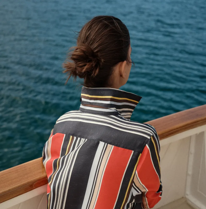 Person sitting on a boat, looking at the water, wearing a striped shirt.
