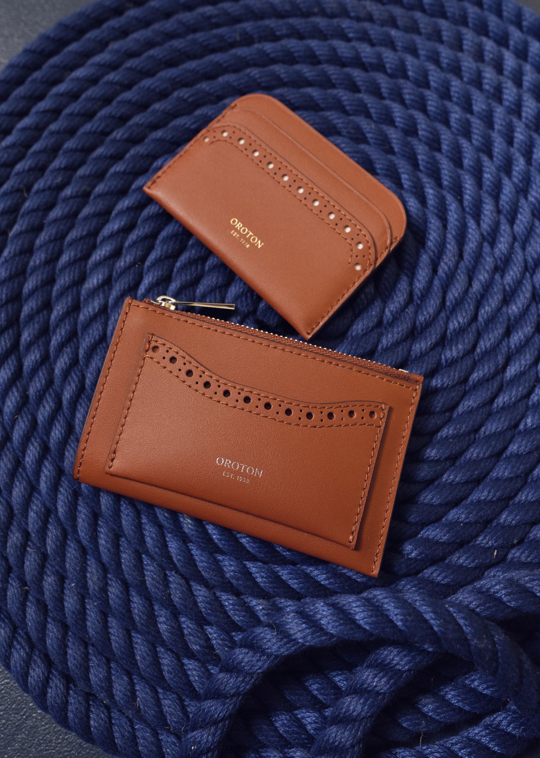 Two brown leather wallets on a navy blue rope background.