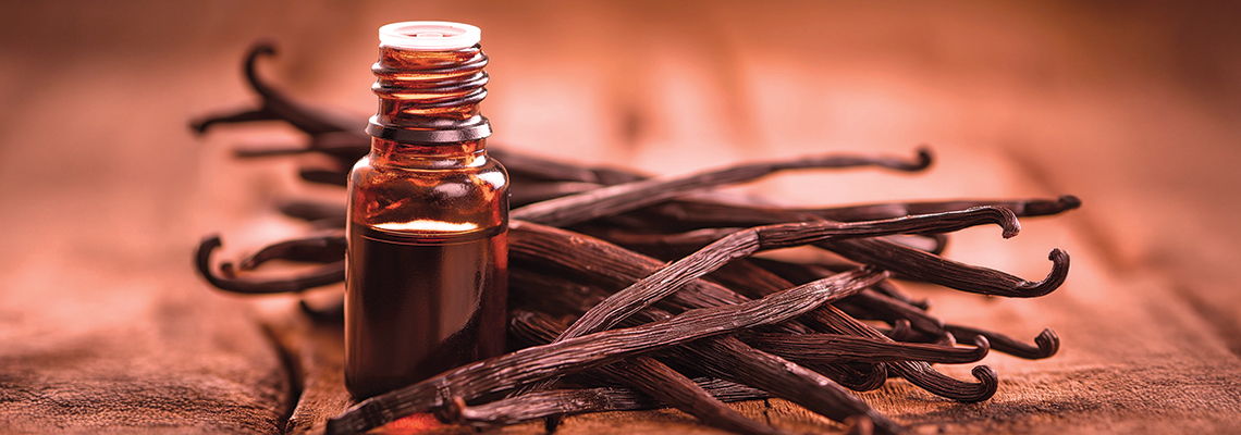 Bottle of vanilla extract surrounded by vanilla pods on a wooden surface.