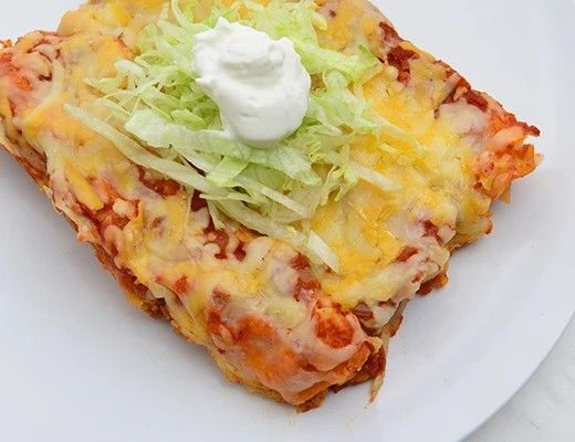 A serving of cheesy enchiladas topped with lettuce and sour cream.
