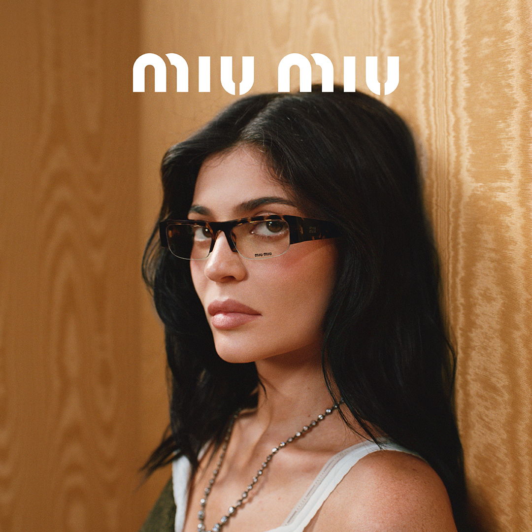 A woman with glasses poses against a wooden background, featuring Miu Miu branding.