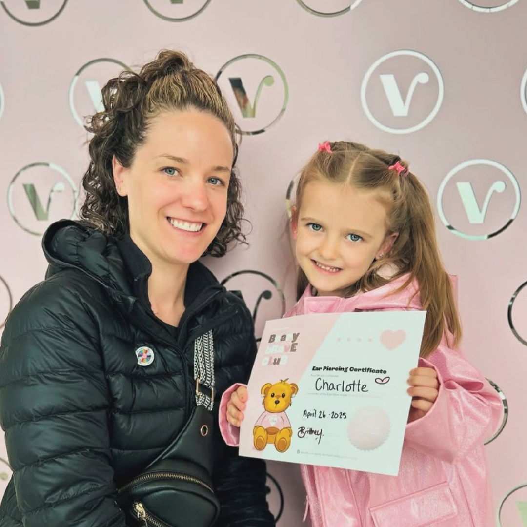 A woman and a girl holding a certificate against a pink background.