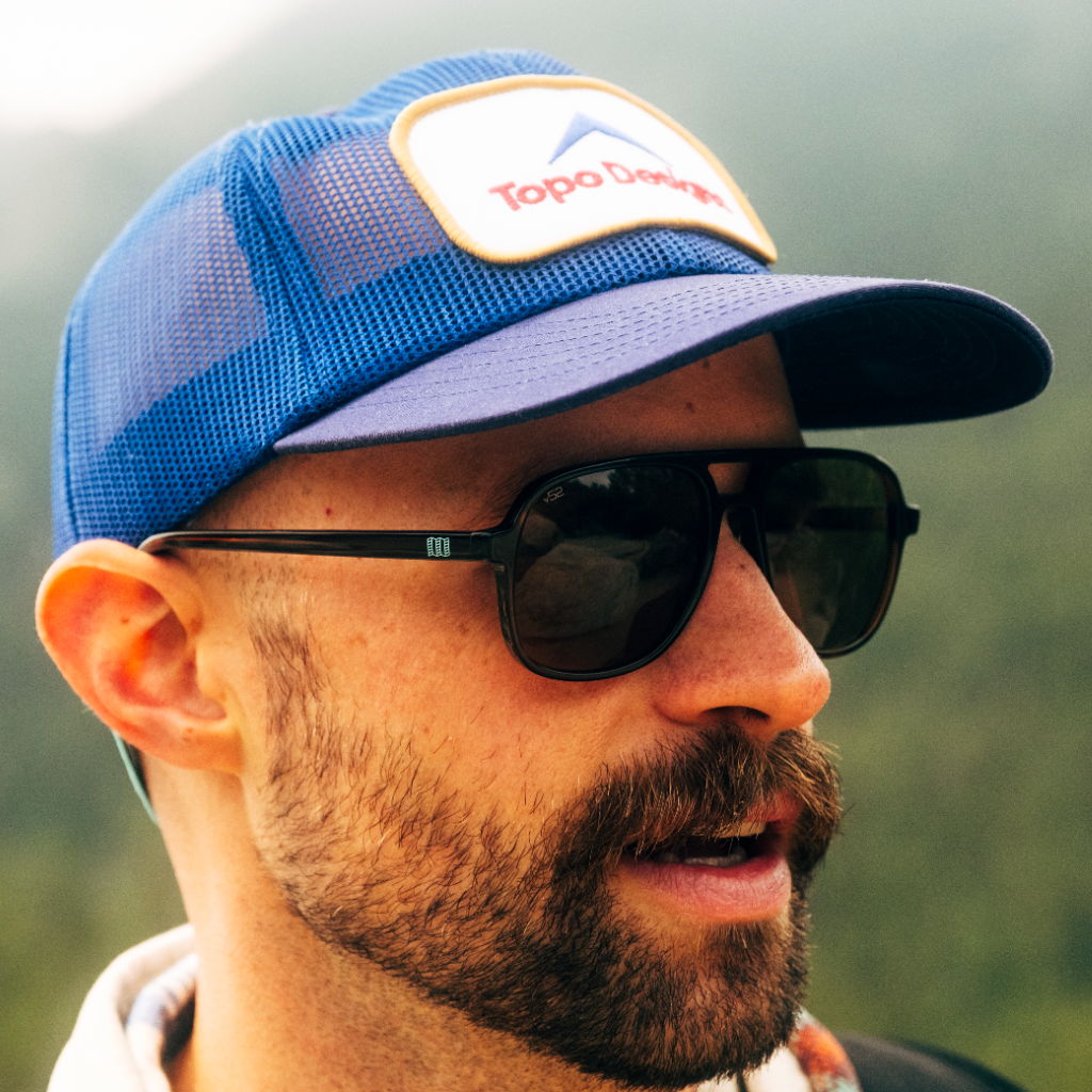 Man wearing sunglasses and a blue cap in an outdoor setting.