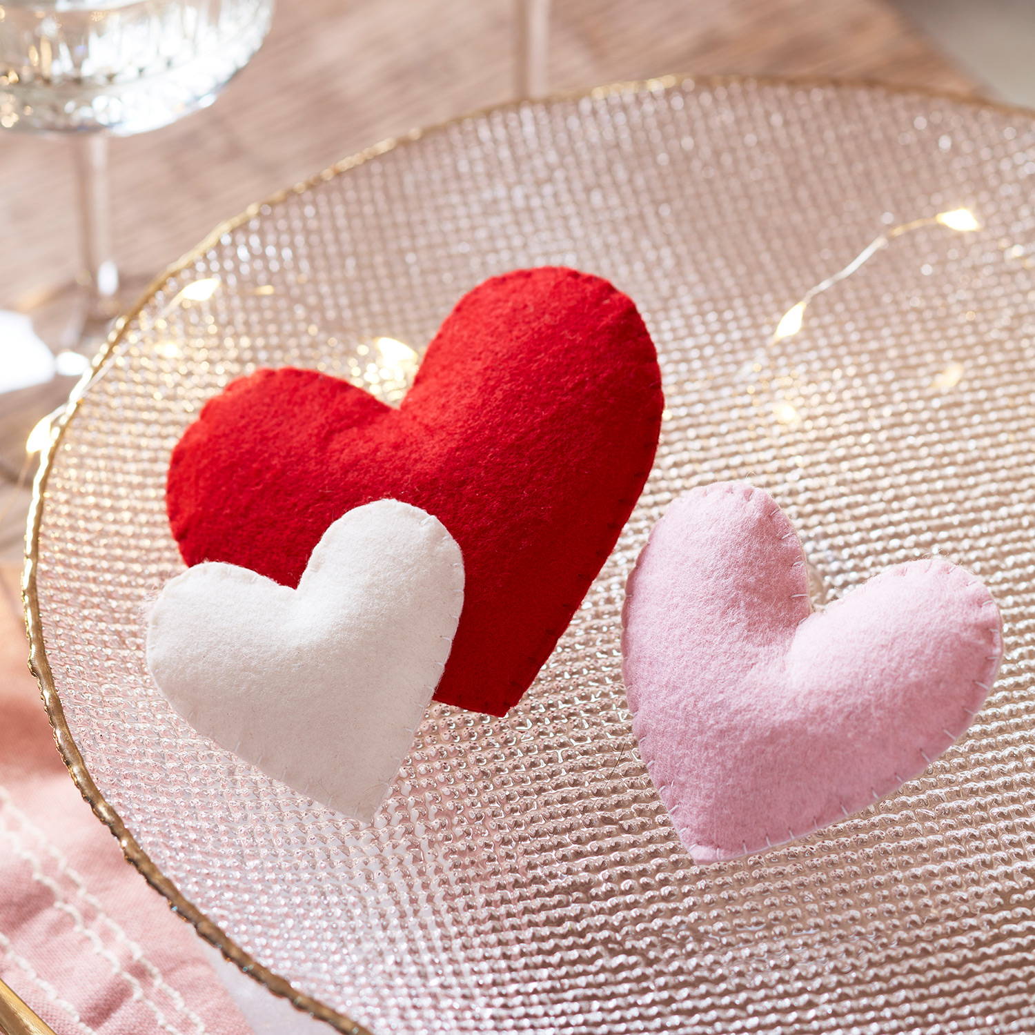 3 felt heart decorations in oink, red and cream in a dish with micro lights.