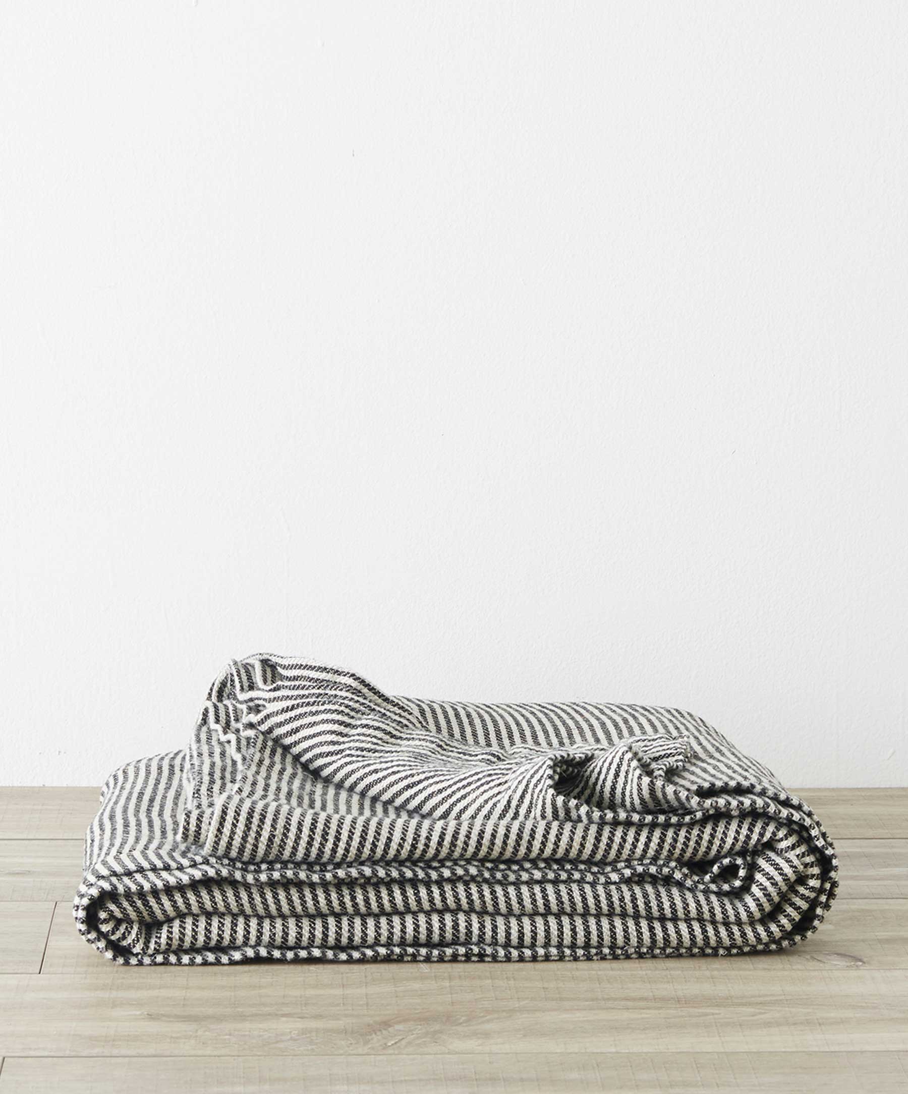 Mira Linen Bedcover - Ellis Stripe folded neatly on wooden floor, showcasing soft, breathable linen The beauty of home