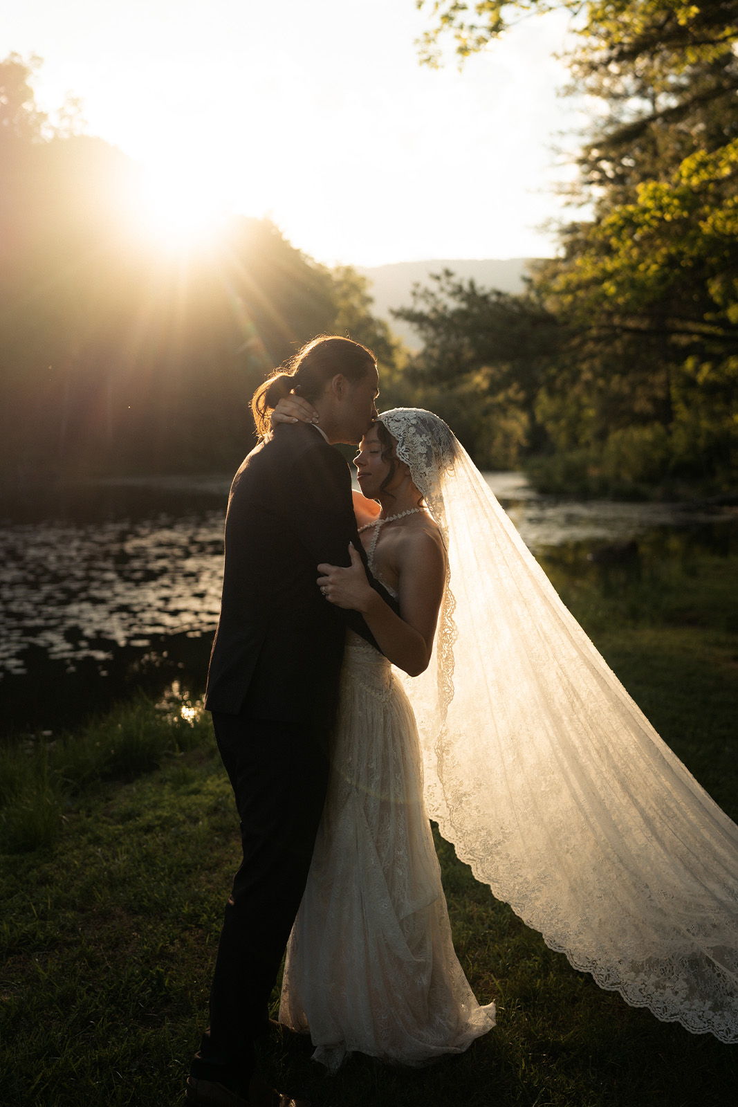 Bride and groom sharing a kiss during sunset by a serene pond.