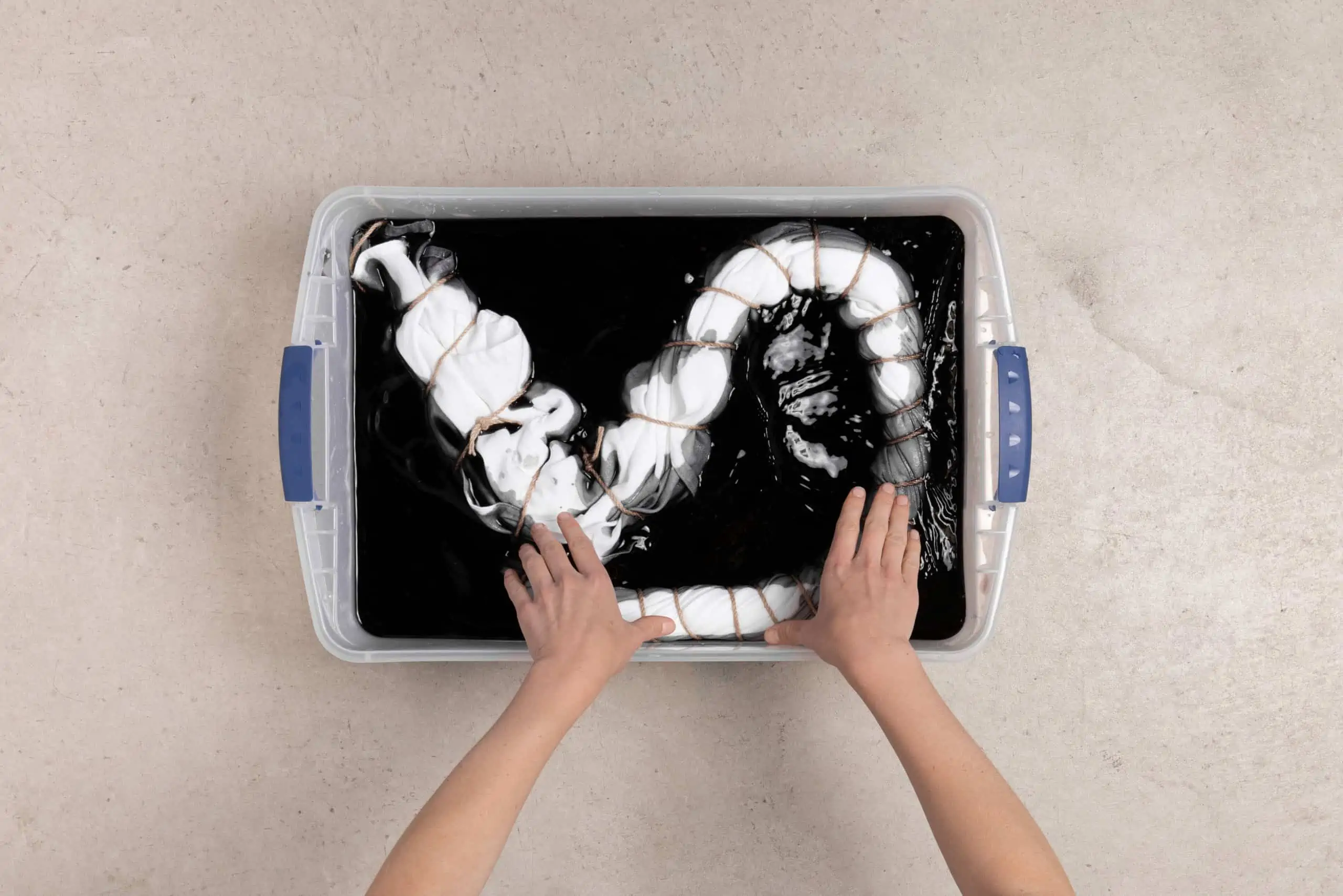 Hands playing with a white, squiggly substance in a black tray.
