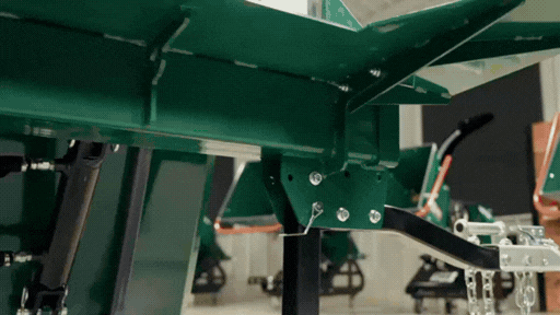 Close-up of a green agricultural machine part in a workshop setting.