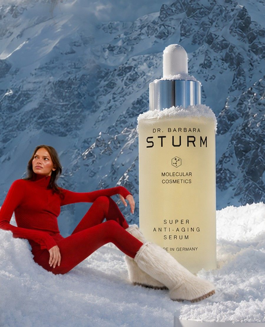 A woman in red poses beside a skincare product in a snowy landscape.