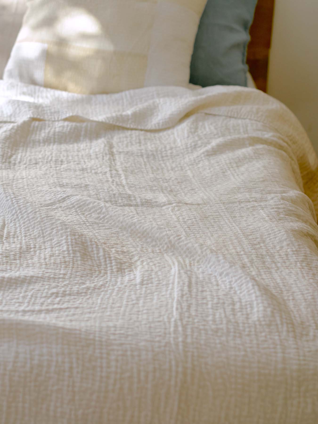 A neatly made bed with a light-colored quilt and a blue pillow.